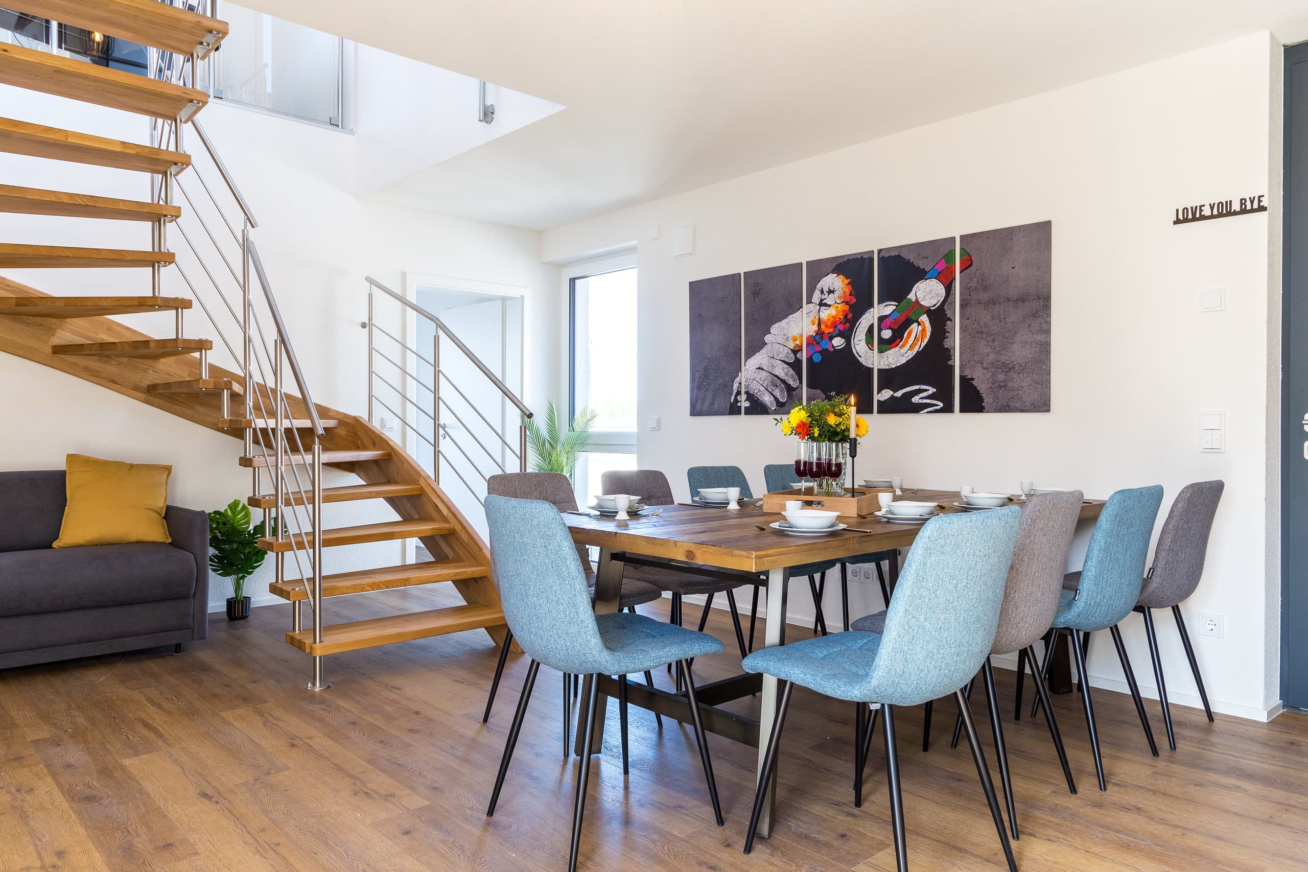 Essbereich mit Holztisch, blauen Stühlen und offener Treppe